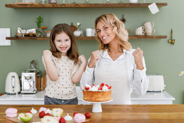 Happy fun chef cook baker mom woman in white shirt work with baby girl helper do winner gesture at kitchen table home Cooking food process concept. Mommy little kid daughter prepare fruit sweet cake