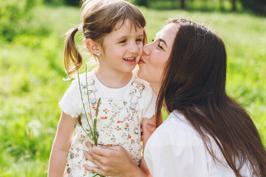 Happy lovely smiling young woman in white clothes have fun with cute child baby girl 5-6 years old Mommy play rest with little kid hug kiss daughter outdoor together. Mother's Day love family concept