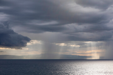 Naklejka na ściany i meble Sun breaking through storm clouds over the ocean