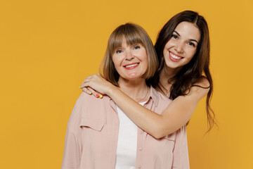 Two young smiling happy satisfied daughter mother together couple women wearing casual beige clothes looking camera isolated on plain yellow color background studio portrait. Family lifestyle concept