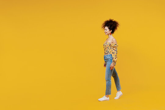 Full length side view young happy smiling fun trendy fashionable woman 20s with culry hair wearing casual clothes walk go isolated on plain yellow background studio portrait. People lifestyle concept