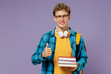 Young boy teen student wear casual clothes backpack headphones glasses hold books show thumb up isolated on plain pastel violet background studio Education in high school university college concept.