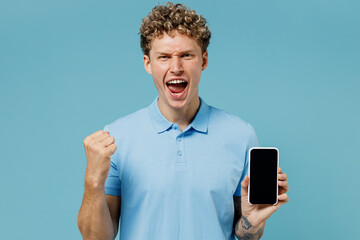 Promoter young curly man 20s years old wears azure t-shirt hold use mobile cell phone with blank...