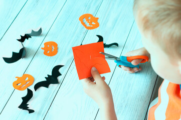 Halloween holiday concept, child carves paper figures of pumpkin and bats. High quality photo