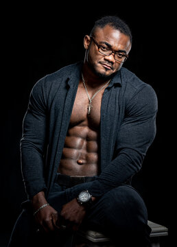 En Portrait of the african american bodybuilder man with shirtless muscular torso. Male wearing jeans isolated on black background