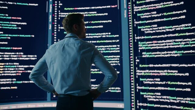 Innovative Startup: Thoughtful Software Engineer Finding Solution, Doing Data Analysis with Big Screen Background. Programmer Developing Futuristic e-Commerce App. Dramatic Back View Handheld