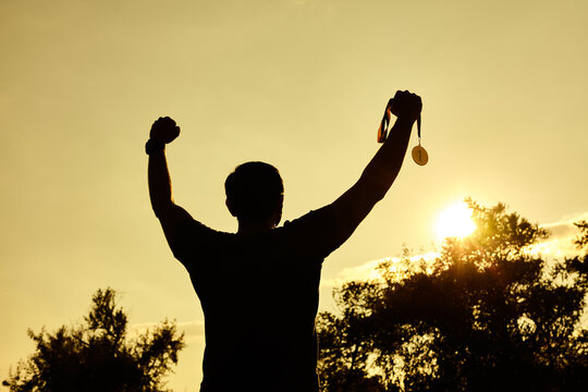 Silhouette people victory raising hands and holding gold medal with sunset sky.
