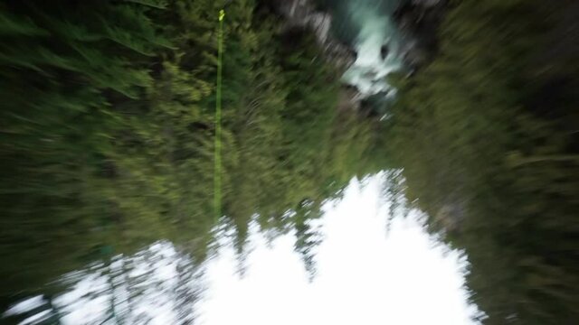 Tilt Down Panning Shot Of Tourist Bungee Jumping Over River In Forest During Vacation - British Columbia, Canada