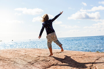 Child does gymnastics and jumps in front of ocean.
Child stands on rocks by the water and feels...