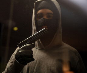 Armed criminal with balaclava holds gun in leather gloved hand. Shooting, killing, violence.