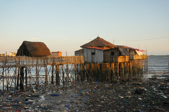 Obama Restaurant on stilts over the water, but a lot of dirty trash around at low tide. Evening, the last rays of the sun. Conakry, Guinea.