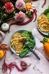 Zucchini pancakes with spinach and avocado in blue plates on the table with a bouquet of autumn dahlias. Dinner table setting with a bouquet of flowers. Flat lay.