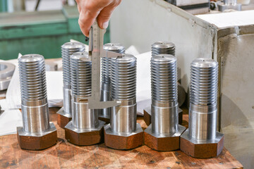 The worker measures the length of the thread on the bolt with a vernier caliper, after turning....