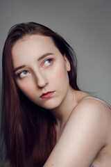 Obraz premium Portrait of a gentle serious gray-eyed girl on a gray background. Perfect porcelain skin. Long chic hair. Expressive look 