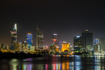 Obraz na płótnie Canvas Colorfuly illuminated towers of Ho Chi Minh city from water at night