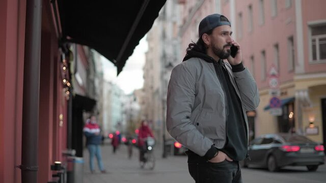 Young, man talking on the phone on the street of a town on a sunny spring day.