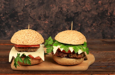 Two cheeseburgers with fresh parsley leaves, tomatoes, cream cheese, onions and cutlet on an old wooden board, food delivery, advertising of a cafe, restaurant, menu, low key,