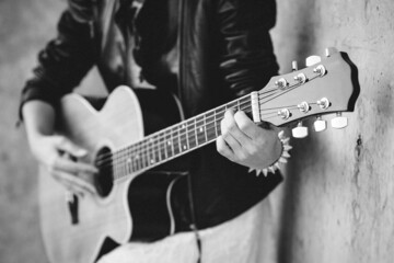 Grayscale photo of man playing guitar beside wall