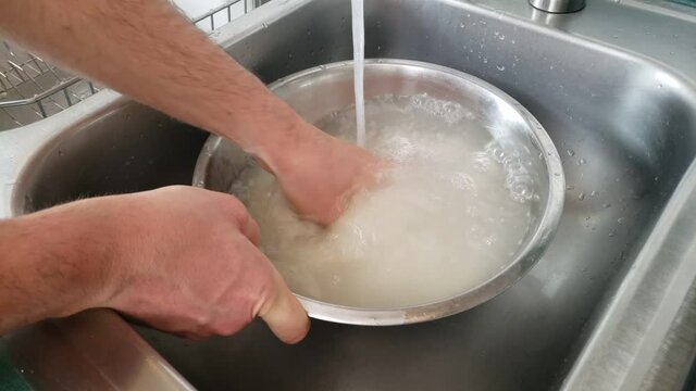 Home Cooking - Washing While Checking White Rice In Stainless Steel Bow Under Running Tap Water In The Sink.