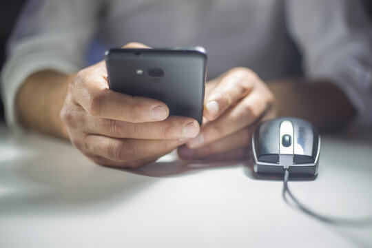 Man in dress shirt using smartphone beside computer mouse