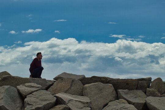 Man in red jacket standing on top brown rock looking at the horizon in the mountain