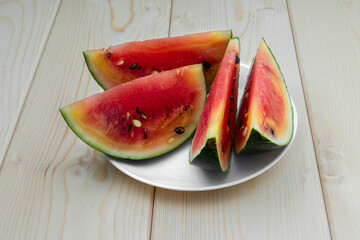 slices of watermelon in a white plate lie on a wooden table