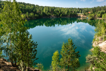 Turquoise lake in the middle of rocky shores and forest with reflective sky and clouds.