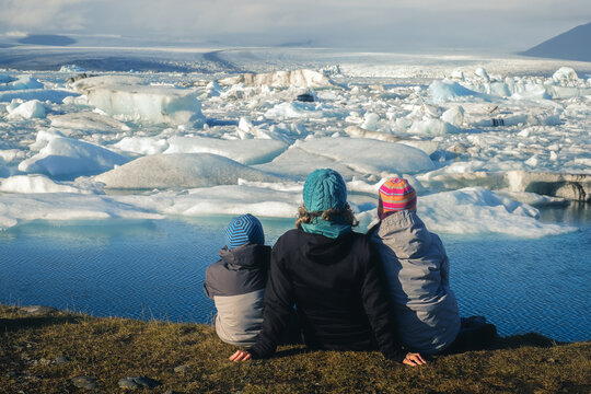 Mother and two children wearing winter clothes sitting on the edge and looking at polar ice caps