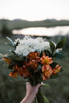 Person holding a white and orange flower bouquet next to a lake
