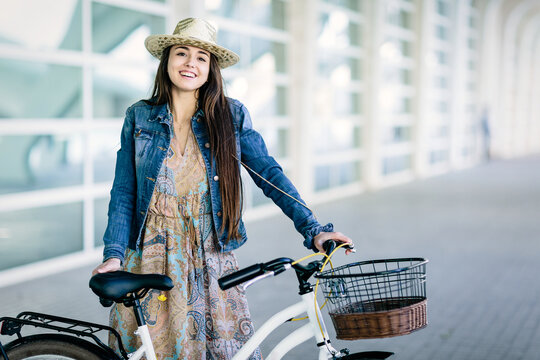 Portrait of a woman with a hat smiling and standing beside a bicycle