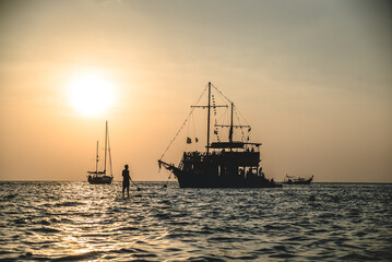 Silhouette of man near sail boat and a ship during sunset