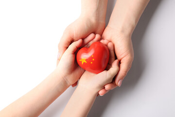 Hands of woman and child with small heart in colors of Chinese flag on white background