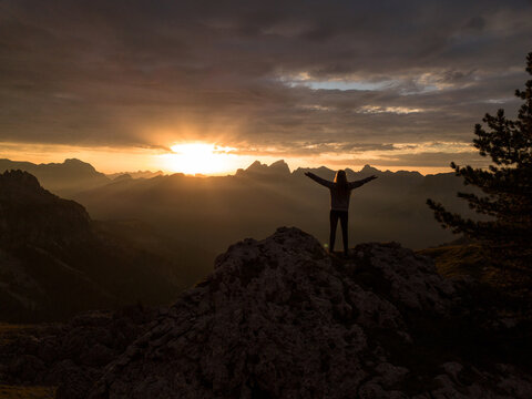 silhouette of person raising arms on top of the mountain during sunset