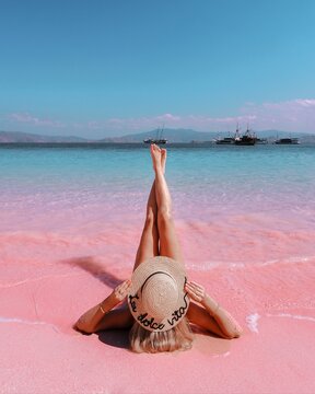 Woman In Brown Sun Hat Lying On Pink Beach In Indonesia