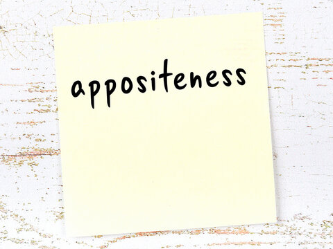 Yellow sticky note on wooden wall with handwritten word appositeness