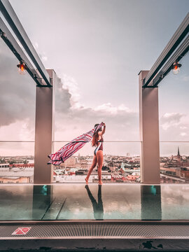 woman in monokini standing near clear glass fence beside swimming pool on rooftop of skyscraper
