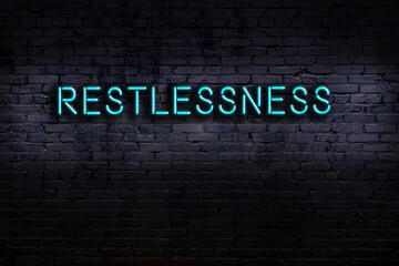 Night view of neon sign on brick wall with inscription restlessness