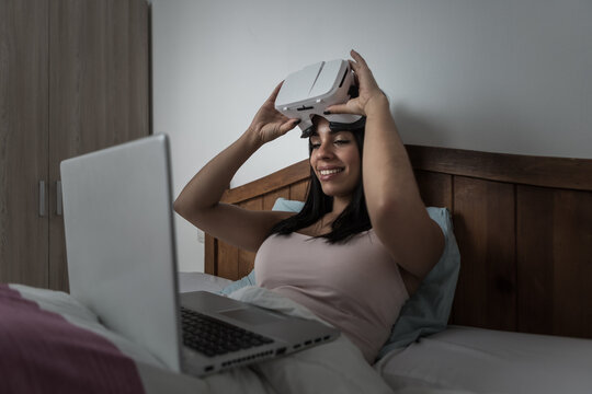 Woman using laptop and VR headset in bed