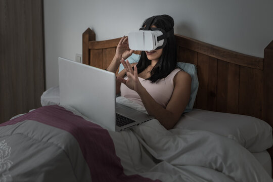 Woman using laptop and VR headset in bed