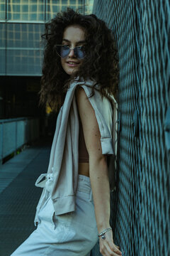 Woman With Curly Hair Wearing Blue Sunglasses Leaning On Fence