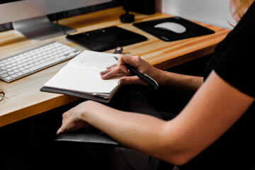 Woman writing a note while working on desktop computer