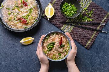 Woman eating tasty Chinese soup with chicken on dark background