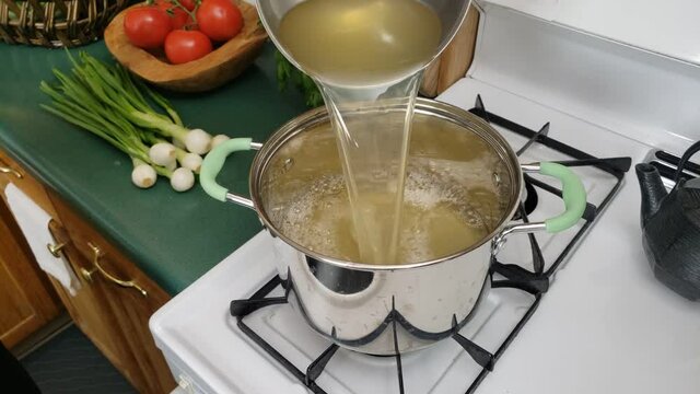 Home cooking - Pouring chicken stock or broth into pot and then adding white rice to be cooked on gas stove.
