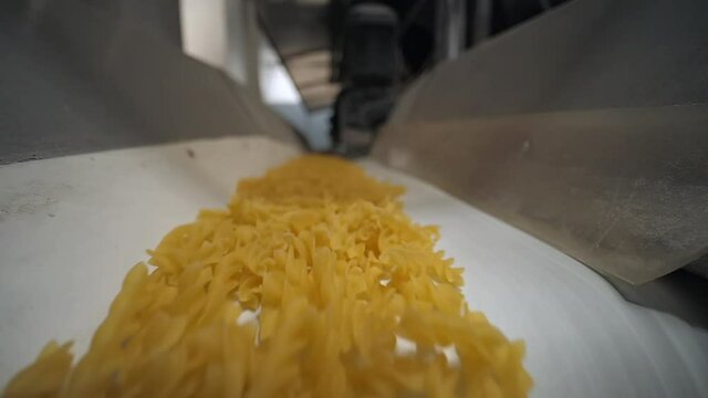Close shoot of a long conveyor belt move with manufactured pasta spirals to a packing department at food industry factory with automatic production lines