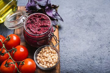 Composition with jar of tasty pesto sauce and ingredients on dark background, closeup