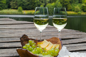 Picnic at the wooden pier by the lake with food, fruit and white wine. Picnic for two, romantic outdoor recreation