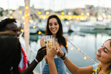 Happy multiracial young people cheering with champagne on a boat during christmas holidays - Millennial friends celebrate birthday together - Friendship, eve and celebration concept