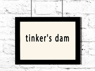 Black frame hanging on white brick wall with inscription tinker's dam - obrazy, fototapety, plakaty