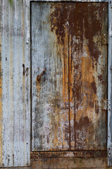 Old industrical metal door on abandoned building with various rust patterns on it.