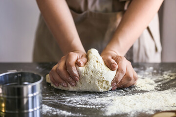 Female chef preparing dough on kitchen table, closeup